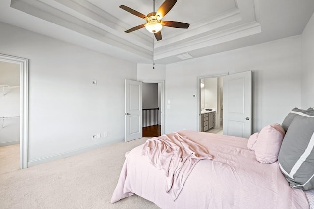 carpeted bedroom featuring a raised ceiling, a spacious closet, ceiling fan, ensuite bath, and baseboards