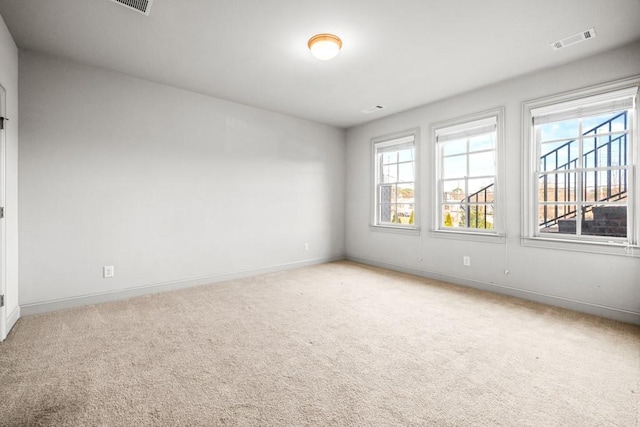 spare room featuring light carpet, a healthy amount of sunlight, baseboards, and visible vents