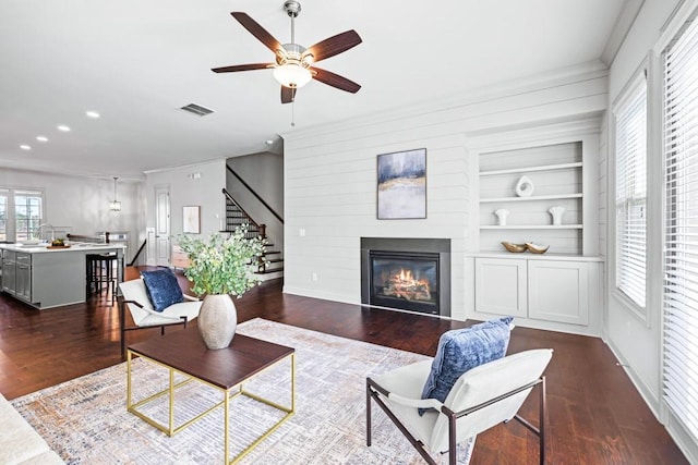 living room featuring dark wood-type flooring, a glass covered fireplace, visible vents, and built in features