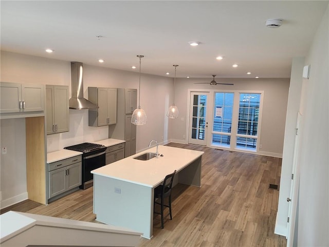 kitchen with stainless steel gas range, ceiling fan, sink, wall chimney range hood, and pendant lighting