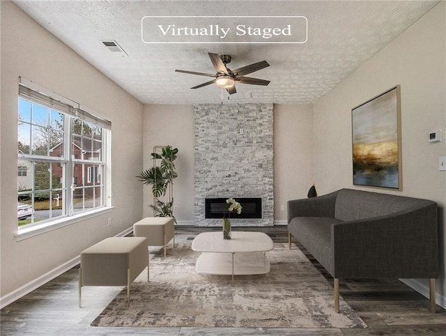 living room with a stone fireplace, ceiling fan, a textured ceiling, and hardwood / wood-style flooring