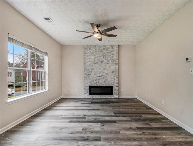 unfurnished living room with a stone fireplace, ceiling fan, dark hardwood / wood-style flooring, and a textured ceiling