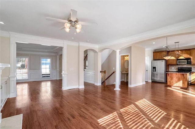 unfurnished living room featuring crown molding, a decorative wall, arched walkways, ceiling fan, and dark wood-type flooring