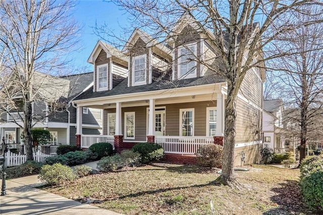 view of front of house with covered porch, brick siding, and fence