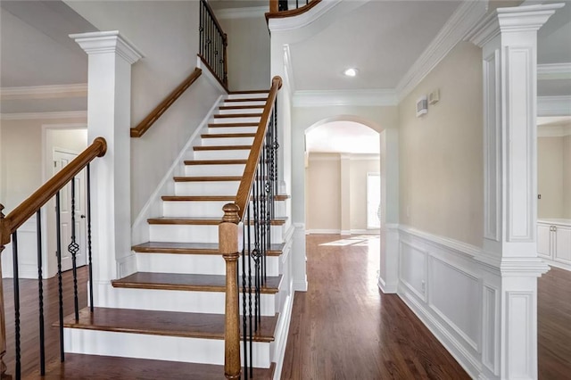 stairs with wood finished floors, wainscoting, a decorative wall, arched walkways, and ornamental molding