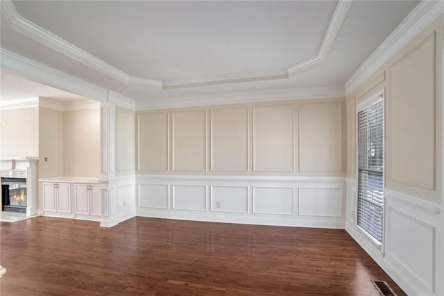 spare room with a decorative wall, visible vents, crown molding, dark wood-type flooring, and a tray ceiling