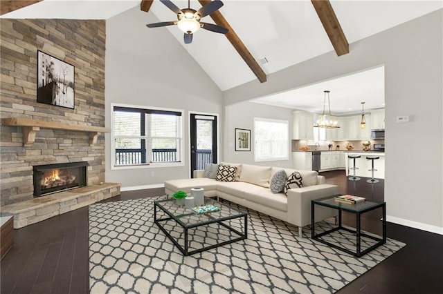 living room featuring ceiling fan with notable chandelier, hardwood / wood-style floors, beam ceiling, high vaulted ceiling, and a stone fireplace