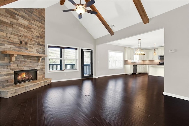 unfurnished living room featuring dark wood-type flooring, ceiling fan with notable chandelier, high vaulted ceiling, a stone fireplace, and beamed ceiling