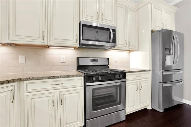 kitchen with stainless steel appliances, dark hardwood / wood-style floors, light stone counters, tasteful backsplash, and cream cabinetry