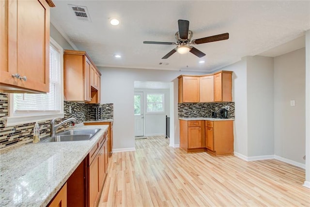 kitchen with sink, backsplash, ceiling fan, light stone counters, and light wood-type flooring