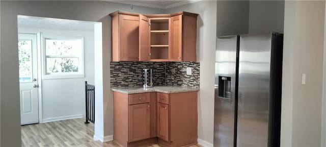 kitchen with light stone counters, decorative backsplash, stainless steel fridge, and light wood-type flooring