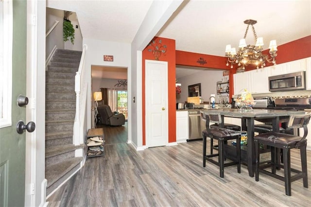 dining space featuring stairway, a chandelier, light wood-style flooring, and baseboards