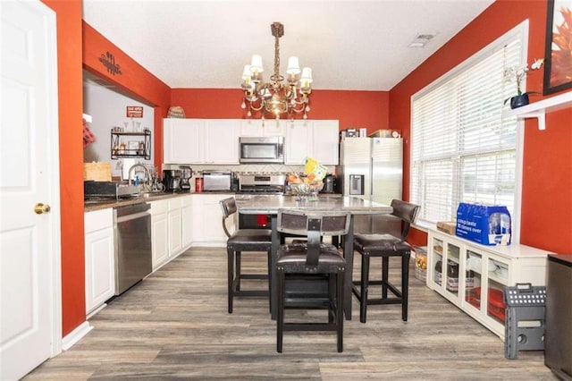 kitchen with stainless steel appliances, a chandelier, white cabinets, decorative backsplash, and wood finished floors