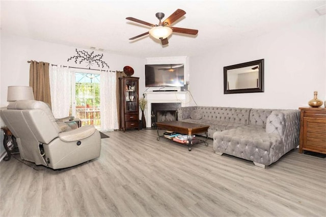 living area featuring wood finished floors, a ceiling fan, and a fireplace