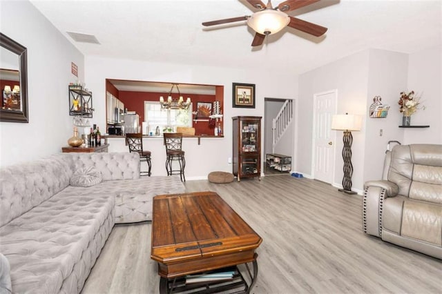 living area featuring stairway, light wood finished floors, a ceiling fan, a chandelier, and baseboards