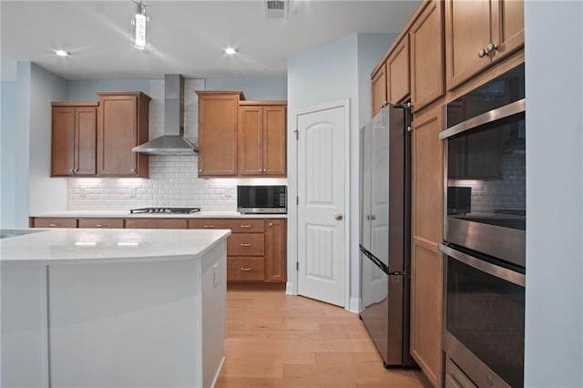kitchen featuring visible vents, backsplash, wall chimney range hood, light wood-style floors, and stainless steel appliances