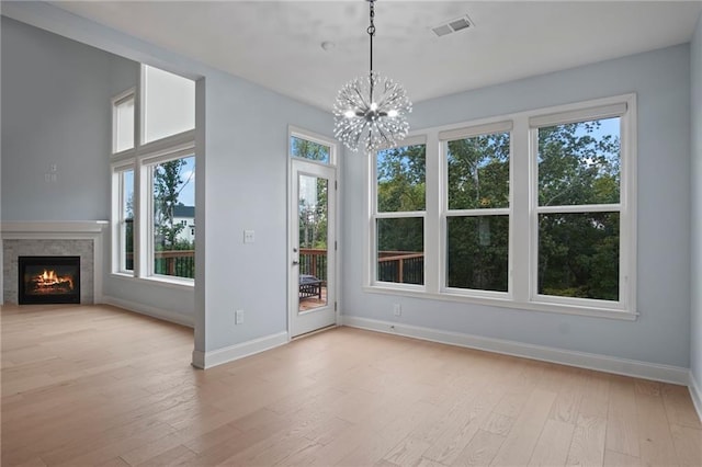 unfurnished dining area with visible vents, baseboards, a warm lit fireplace, light wood-style floors, and a notable chandelier