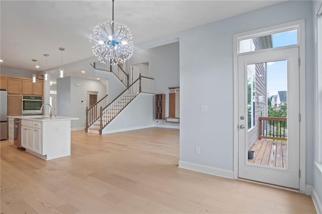 kitchen featuring baseboards, light wood finished floors, a sink, appliances with stainless steel finishes, and decorative light fixtures