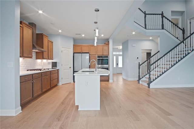 kitchen with light wood finished floors, light countertops, stainless steel appliances, wall chimney exhaust hood, and a sink