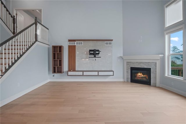 unfurnished living room featuring wood finished floors, visible vents, baseboards, stairs, and a towering ceiling