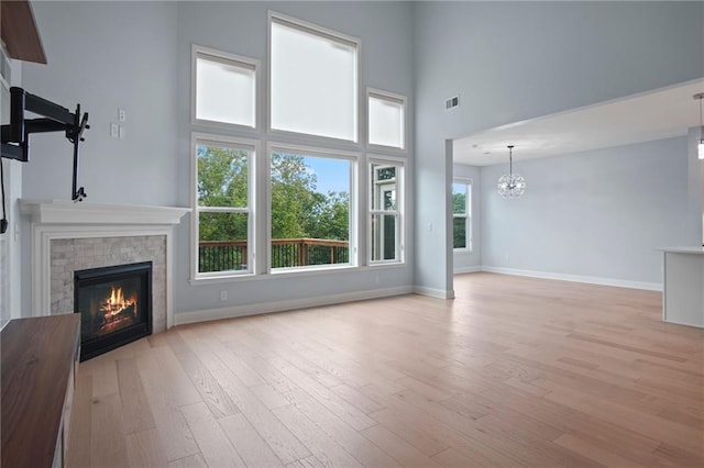 unfurnished living room with visible vents, baseboards, an inviting chandelier, light wood-style flooring, and a brick fireplace