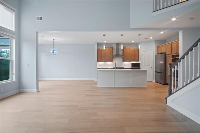 kitchen featuring visible vents, a high ceiling, stainless steel appliances, wall chimney range hood, and brown cabinets