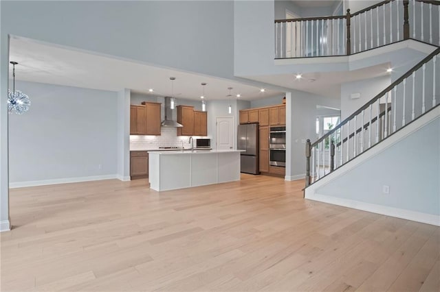 kitchen with wall chimney range hood, brown cabinetry, open floor plan, and appliances with stainless steel finishes