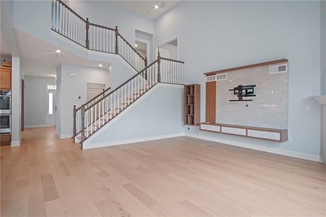 unfurnished living room with stairs, light wood-style floors, and baseboards