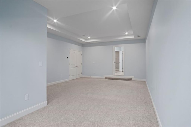 unfurnished room featuring a tray ceiling, recessed lighting, baseboards, and light carpet