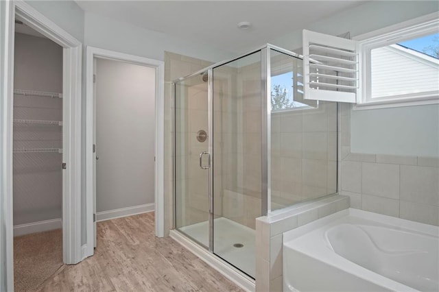 full bath with a walk in closet, a garden tub, wood finished floors, and a shower stall