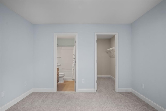 unfurnished bedroom featuring a walk in closet, a closet, connected bathroom, carpet flooring, and baseboards