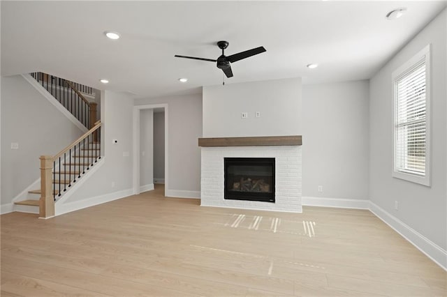 unfurnished living room featuring a ceiling fan, stairway, light wood-style flooring, a brick fireplace, and recessed lighting