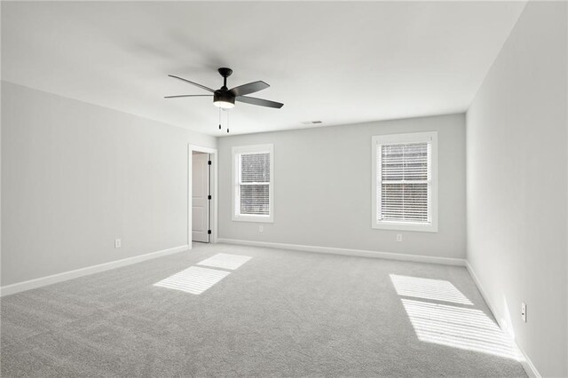 spare room featuring light colored carpet, a ceiling fan, and baseboards