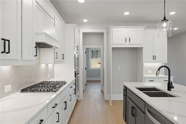 kitchen featuring appliances with stainless steel finishes, premium range hood, a sink, white cabinets, and recessed lighting