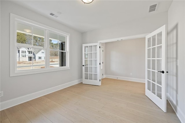 empty room featuring french doors, baseboards, and light wood-style flooring