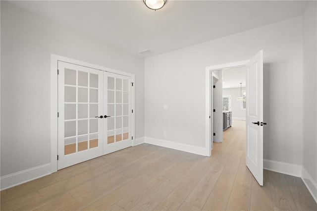 empty room featuring french doors, light wood-type flooring, and baseboards