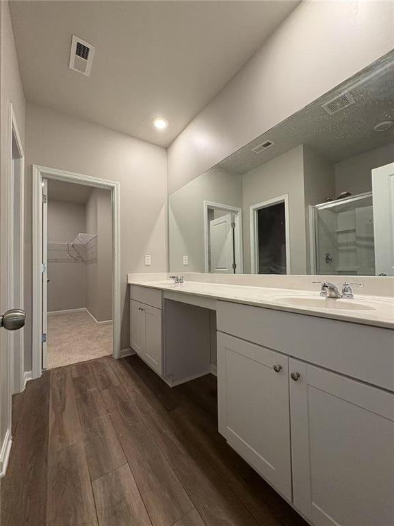 bathroom with wood finished floors, a stall shower, a sink, and visible vents