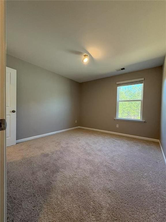 spare room featuring carpet floors, visible vents, and baseboards