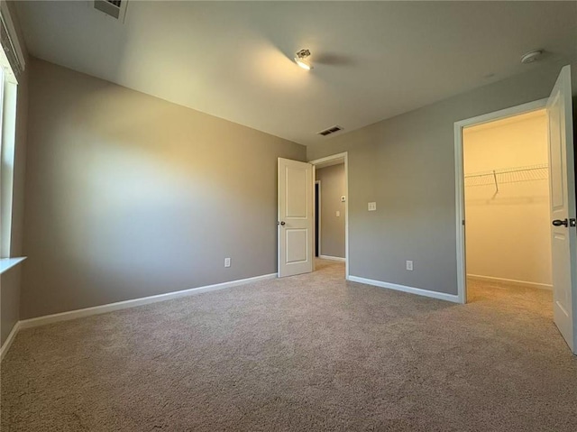 unfurnished bedroom featuring a spacious closet, carpet flooring, visible vents, and baseboards