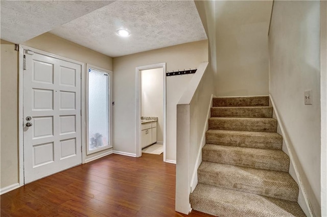 foyer entrance featuring dark wood-style floors, stairs, a textured ceiling, and baseboards