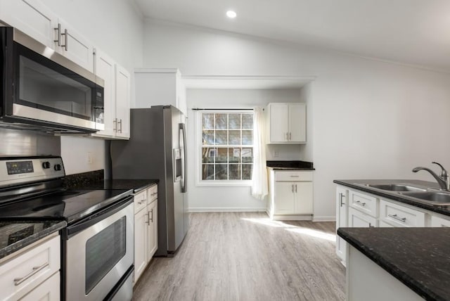 kitchen with dark stone counters, stainless steel appliances, light wood-style floors, white cabinetry, and a sink