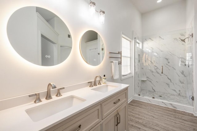 bathroom featuring double vanity, a marble finish shower, a sink, and wood finished floors