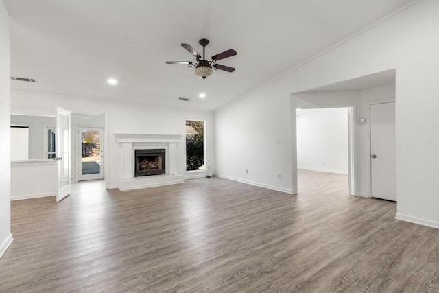 unfurnished living room featuring baseboards, visible vents, a ceiling fan, a fireplace with raised hearth, and wood finished floors