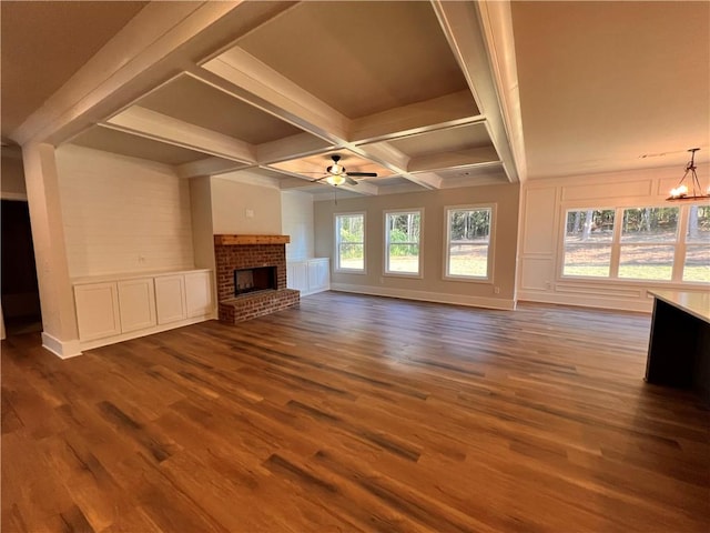 unfurnished living room with coffered ceiling, beam ceiling, dark wood-type flooring, a brick fireplace, and ceiling fan with notable chandelier