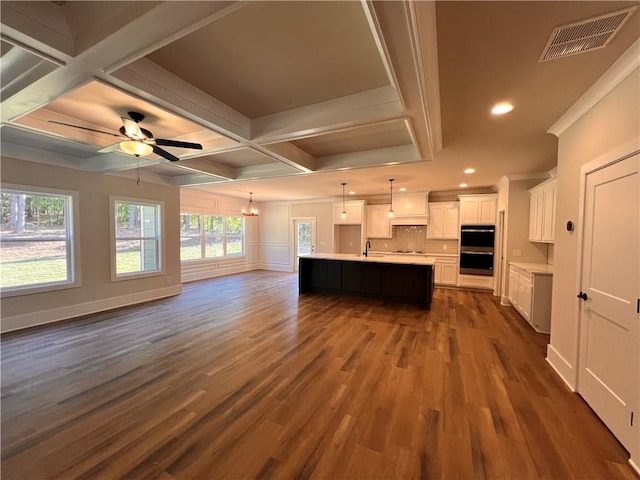 kitchen with coffered ceiling, a kitchen island with sink, dark hardwood / wood-style floors, and white cabinets