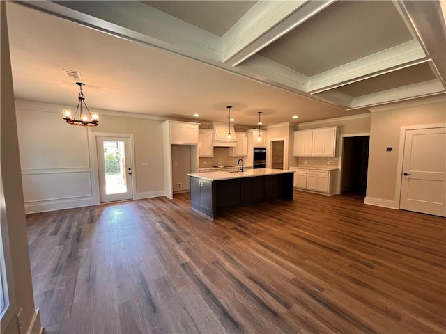 kitchen with a center island with sink, crown molding, white cabinetry, and dark hardwood / wood-style floors