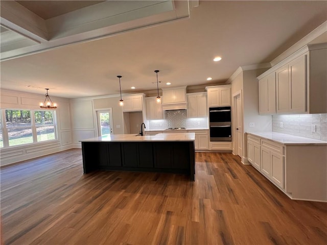 kitchen with white cabinetry, decorative light fixtures, an island with sink, and hardwood / wood-style floors