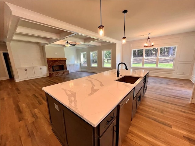 kitchen featuring an island with sink, hardwood / wood-style flooring, dishwasher, decorative light fixtures, and sink