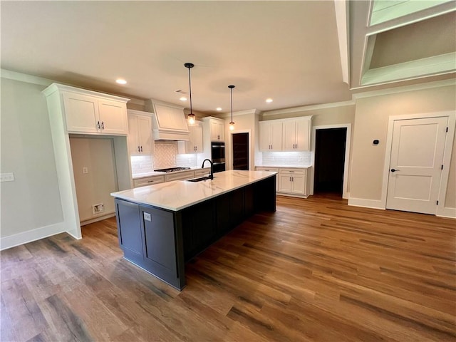 kitchen featuring white cabinets, a center island with sink, dark hardwood / wood-style flooring, crown molding, and decorative light fixtures