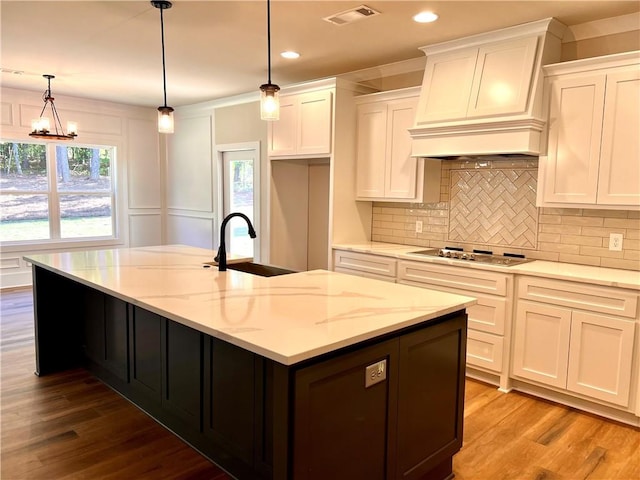 kitchen with white cabinetry, sink, decorative light fixtures, and a kitchen island with sink